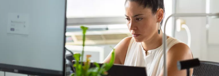 Woman concentrating on work at her desk with a computer and plant.