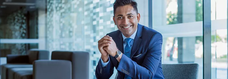 Smiling man in a blue suit sitting in a modern office setting.