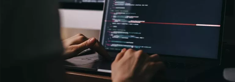 Person typing code on a laptop in a dimly lit room.