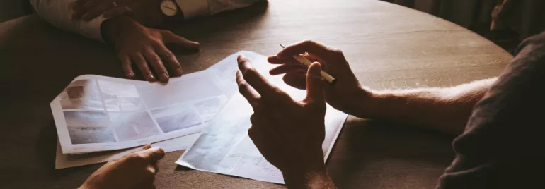 People discussing papers around a wooden table.