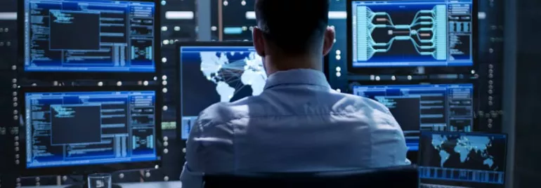Person working at a desk with multiple computer monitors displaying data and maps.