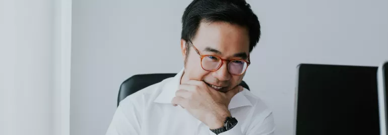 Man in glasses smiling at a desk with two computers.