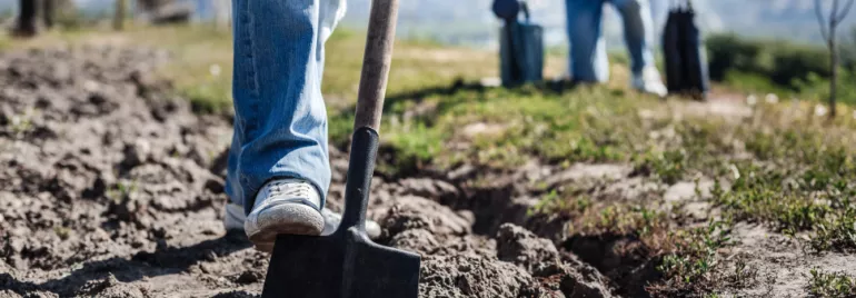 Close-up of a person digging soil with a shovel on a sunny day.