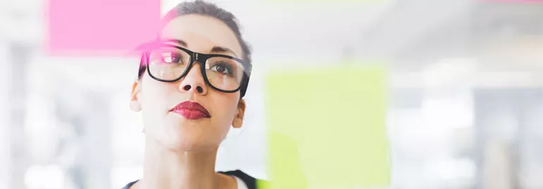 Person with glasses looking at colorful sticky notes on glass.