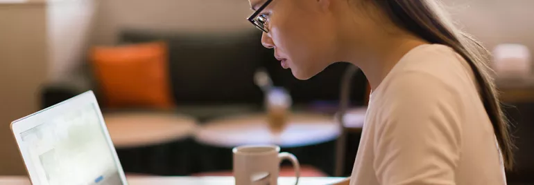 Person with glasses focused on a laptop in a cozy cafe.