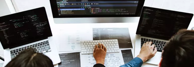 Three people collaborate on laptops with code on screens at a desk.