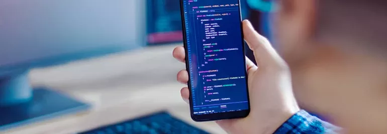 Person holding a smartphone displaying code, with a computer keyboard in the background.