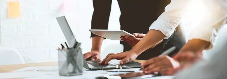 Group of people working together on laptops and tablets at a desk.