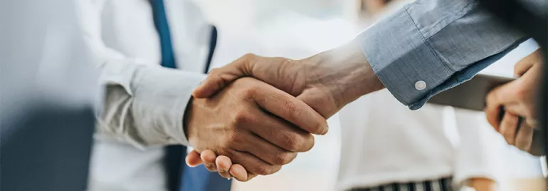 Two people in business attire shaking hands in a close-up view.