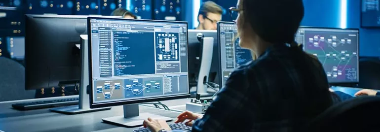 Person working on multiple computer screens in a dark office.