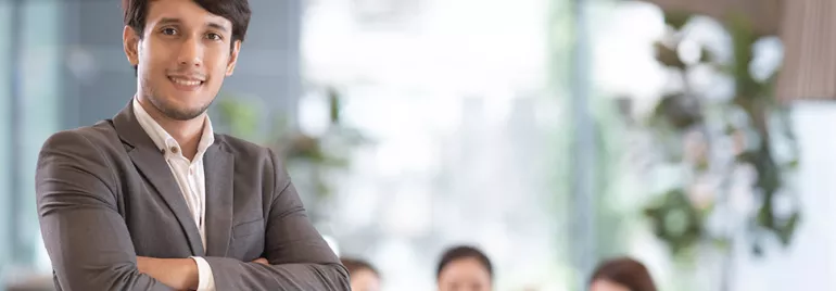 Confident businessman with arms crossed, standing in a bright office.