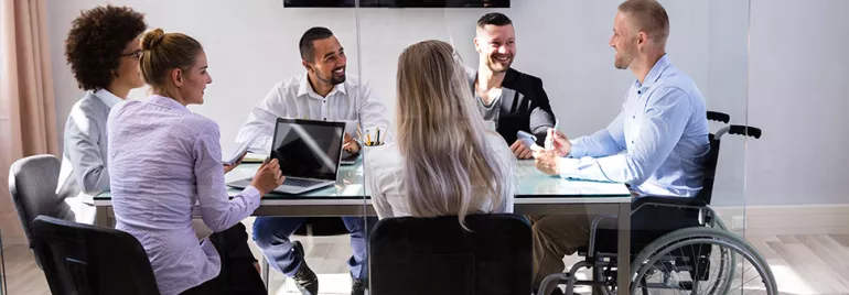 A diverse group of colleagues smiling in a meeting around a glass table.