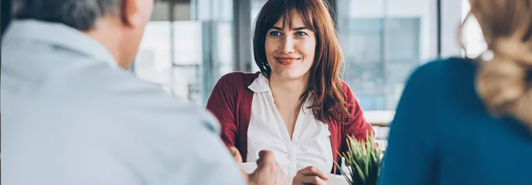 Woman smiling in a meeting with two people in an office setting.