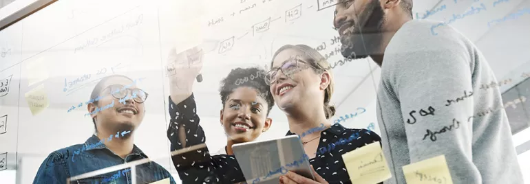 Group of people brainstorming with notes on glass board.