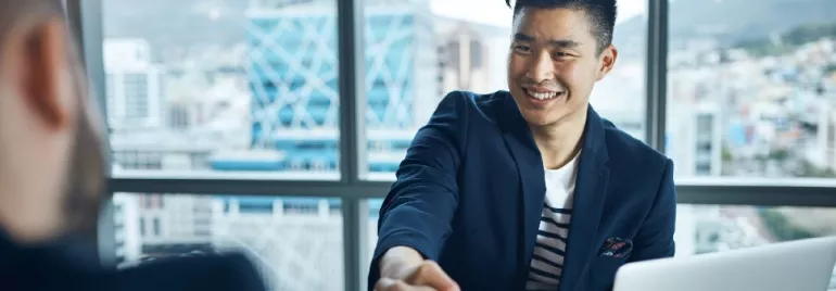 Two people shaking hands in an office with city view in background.