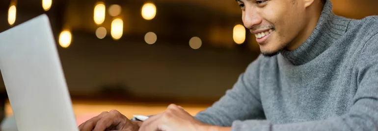 Man in gray sweater smiling while using a laptop.