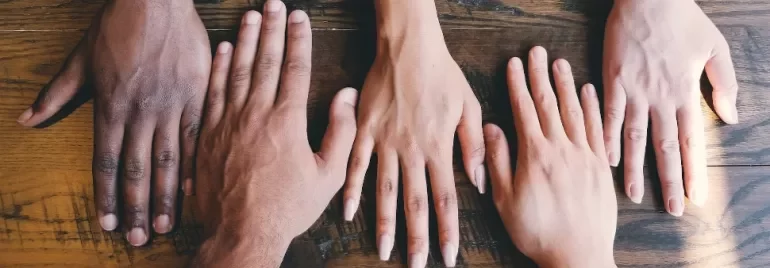 Five diverse hands placed on a wooden table.