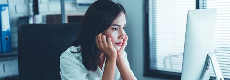 Woman sitting at a desk, looking at a computer screen with focus.
