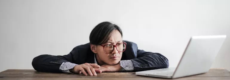 Man with glasses looking at a laptop on a wooden table.