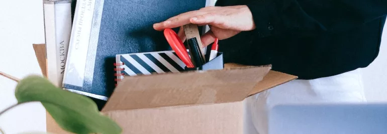 Person packing office supplies in a cardboard box.