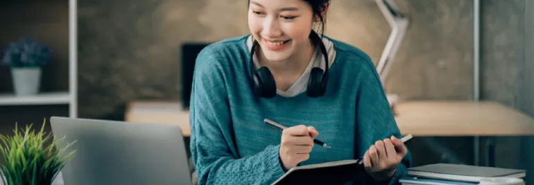 Woman smiling while writing in a notebook at her desk