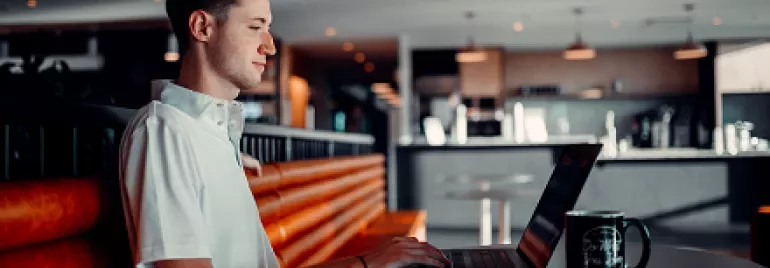 Man working on a laptop in a modern cafe setting.