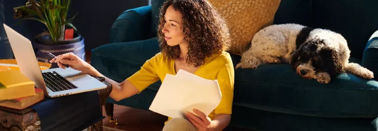 Woman working on a laptop at home with a dog sleeping on the couch.