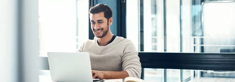 Man smiling while working on a laptop at a desk.