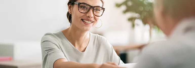Smiling woman with glasses sitting at a table during a conversation.