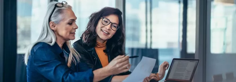 Two women of different age groups and ethnicities looking through a document together