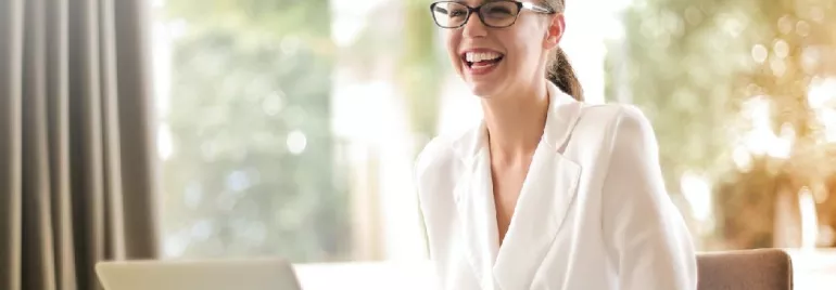 Laughing businesswoman working in office with laptop. Photo by Andrea Piacquadio via Pexels