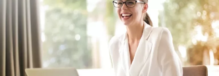 Smiling woman in glasses and a white blazer using a laptop.