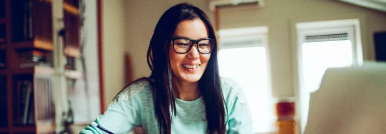 Smiling person with glasses using a laptop at home.