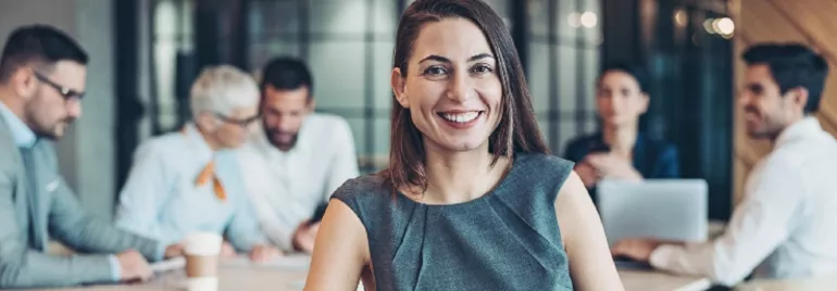 Smiling woman in a business meeting with colleagues in the background.