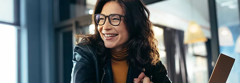 Person in glasses smiling indoors, wearing a leather jacket.