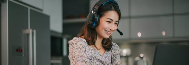 Smiling woman in headphones working on a laptop in a modern kitchen.