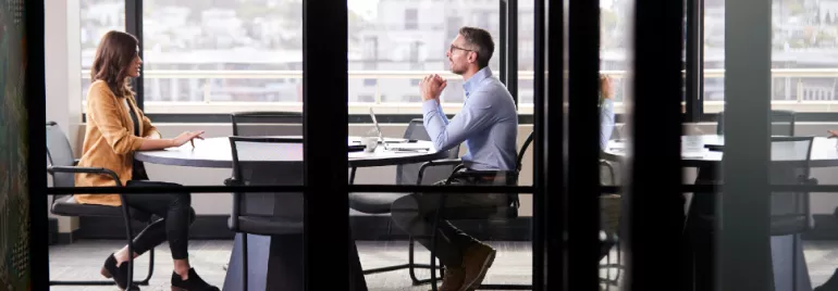 Two people having a meeting in a glass-walled office.