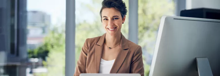 Smiling woman at her desk with a computer in a modern office.