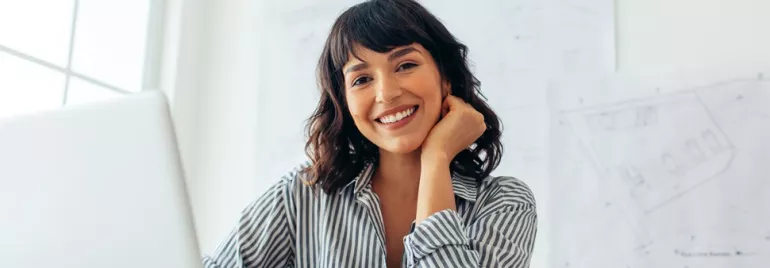 Smiling person in a striped shirt at a desk with architectural plans.