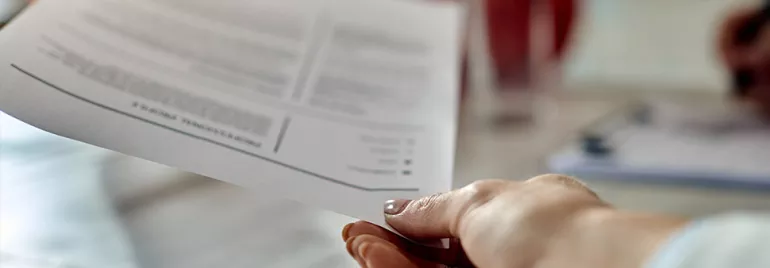 Close-up of a person's hand holding a document over a table.