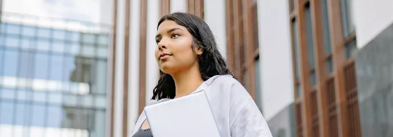 Young woman with a laptop, standing outside a modern building.