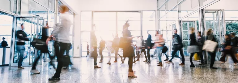Blurred motion of people walking through a busy glass entrance.