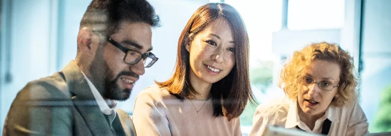 Three people in a meeting, smiling and discussing around a laptop.