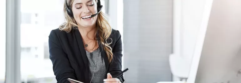 2. A woman wearing a headset holds a notepad, engaged in a discussion or taking notes.