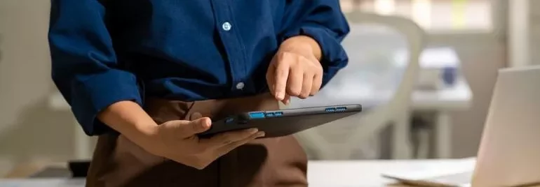Individual displays a tablet in front of a laptop, illustrating the use of multiple technology tools.