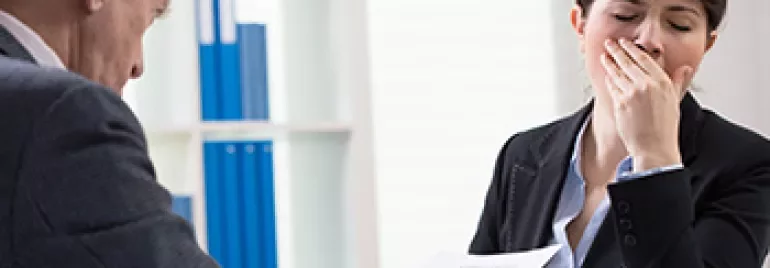 Two people in an office, one holding papers, the other yawning.