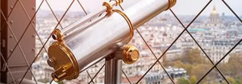 Telescope overlooking city view through lattice fence.