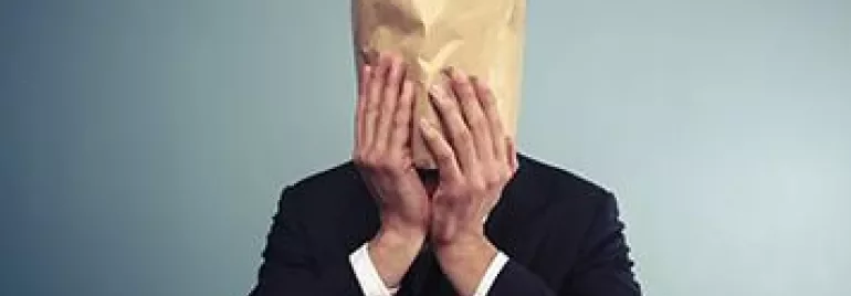 Person in a suit with a paper bag over their head, against a plain background.