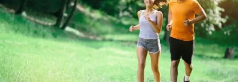 A man and woman jogging on a sunny path surrounded by green trees.