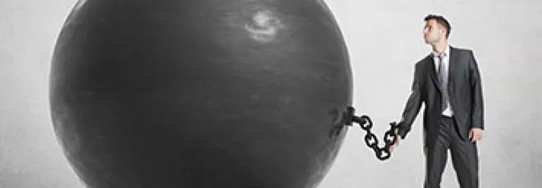 Man in business suit chained to a large black ball.
